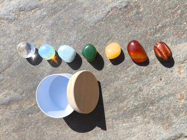 Piedras pulidas del set para los chakras presentadas junto a cuenco sobre superficie de piedra