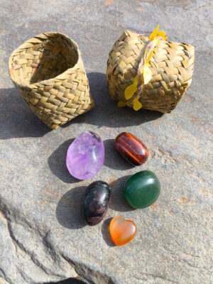 Set de Aries con granate, aventurina, ojo de toro, cornalina y amatista pulidos presentados junto a cesta natural sobre superficie de piedra