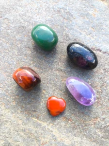 Piedras pulidas del set de Aries con ojo de toro, aventurina, granate, cornalina y amatista dispuestas sobre superficie de piedra