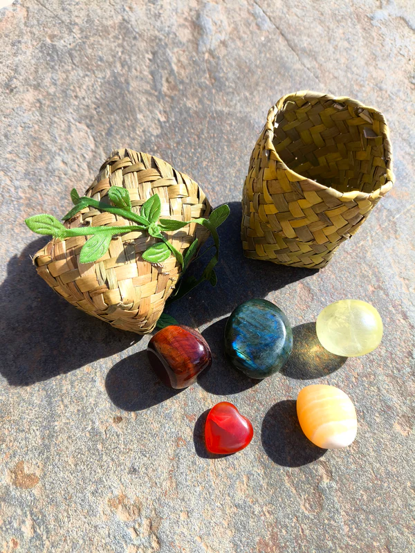 Piedras pulidas del set de Leo con ojo de toro, labradorita, topacio, cornalina y citrino dispuestas junto a cesta natural sobre superficie de piedra