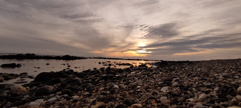 Puesta de sol sobre la costa con reflejos dorados y piedras en primer plano