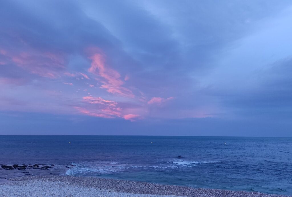Cielo azul con nubes rosadas al atardecer sobre el mar Mediterráneo, simbolizando la energía aire-agua del signo Acuario.