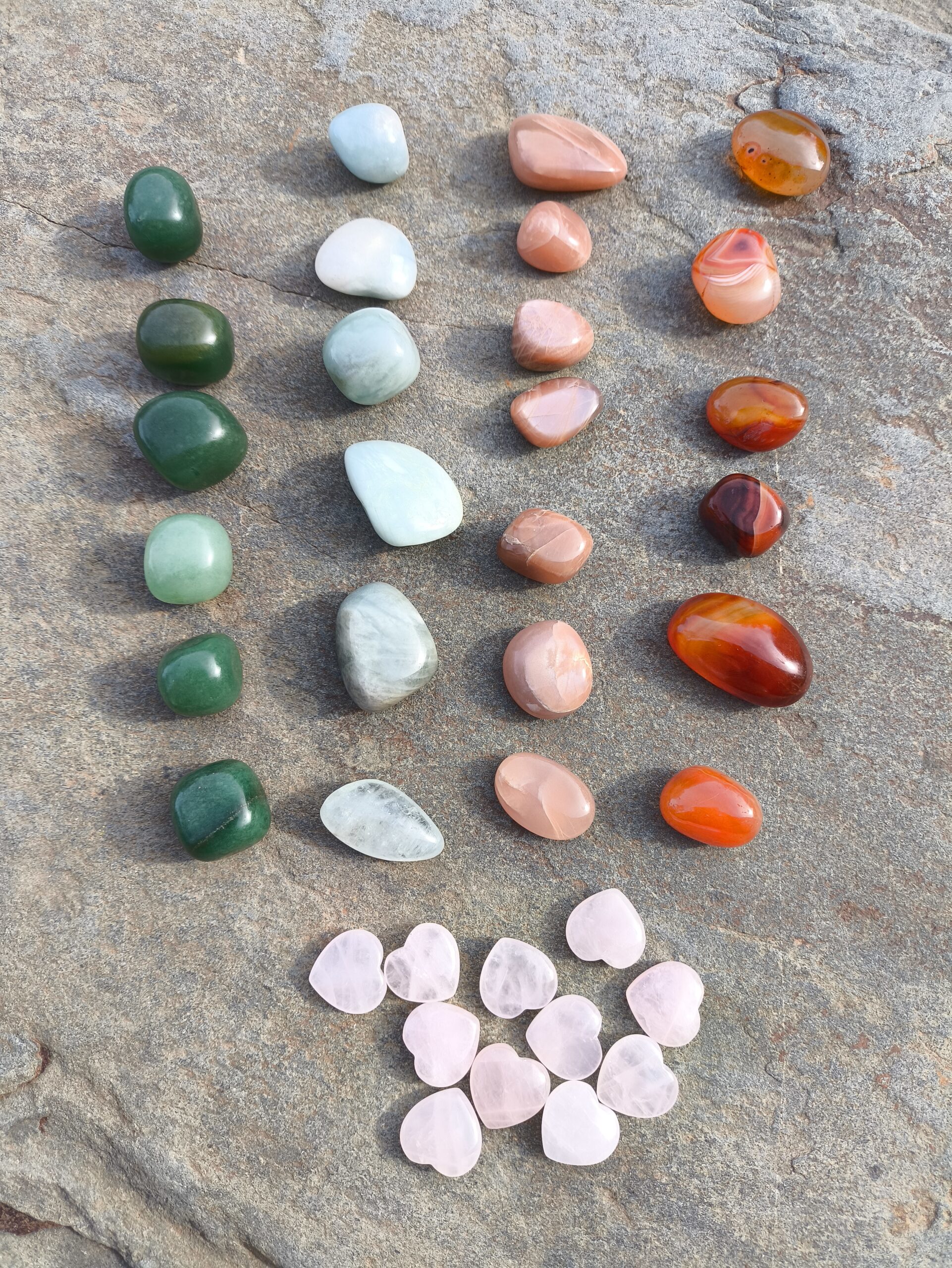 Aventurina, aguamarina, piedra luna melocotón, cornalina y cuarzo rosa pulidos dispuestos en filas sobre piedra