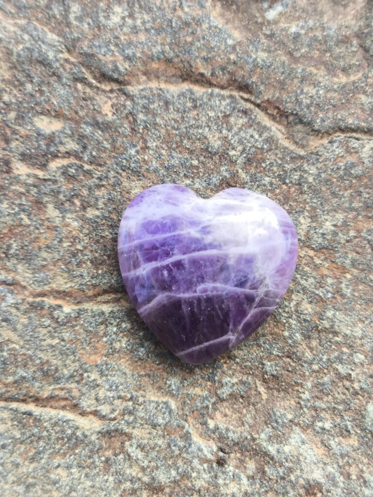 Amatista en forma de corazón sobre roca, tonos morados naturales — piedra para equilibrio emocional y claridad mental.