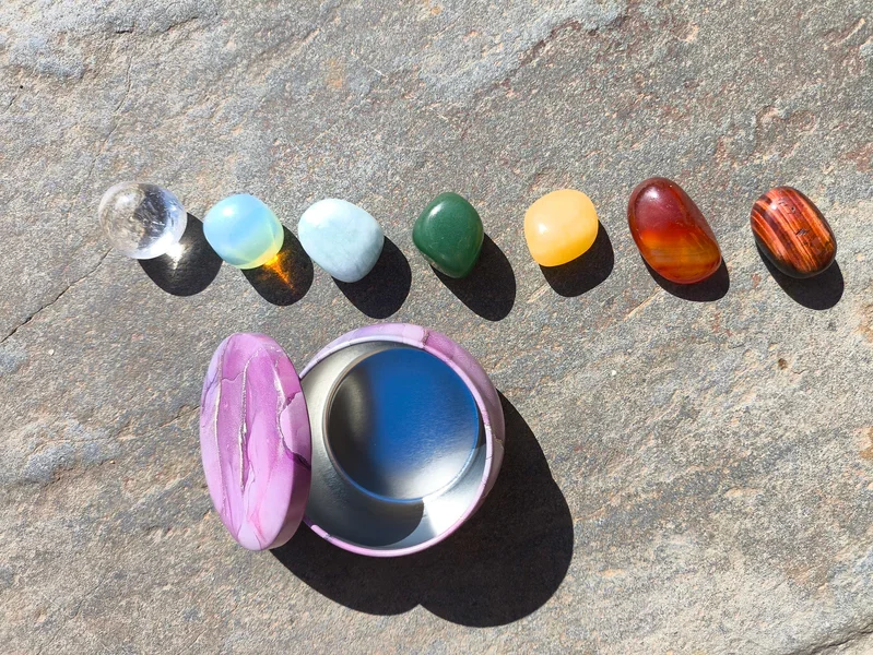 Set para los chakras con siete piedras pulidas alineadas por color, dispuesto sobre superficie de piedra natural