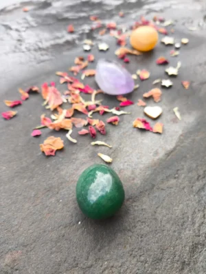 Disposición de piedras pulidas con topacio, aventurina y amatista sobre superficie de piedra con pétalos