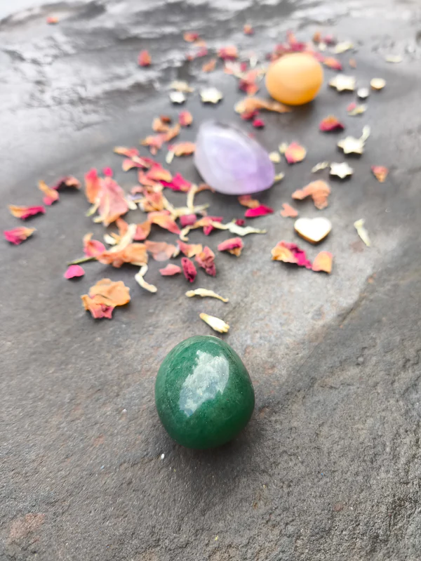 Disposición de piedras pulidas con topacio, aventurina y amatista sobre superficie de piedra con pétalos