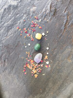 Composición simbólica con piedras pulidas de tonos amarillo, verde y violeta, dispuestas sobre superficie de piedra con pétalos y elementos decorativos