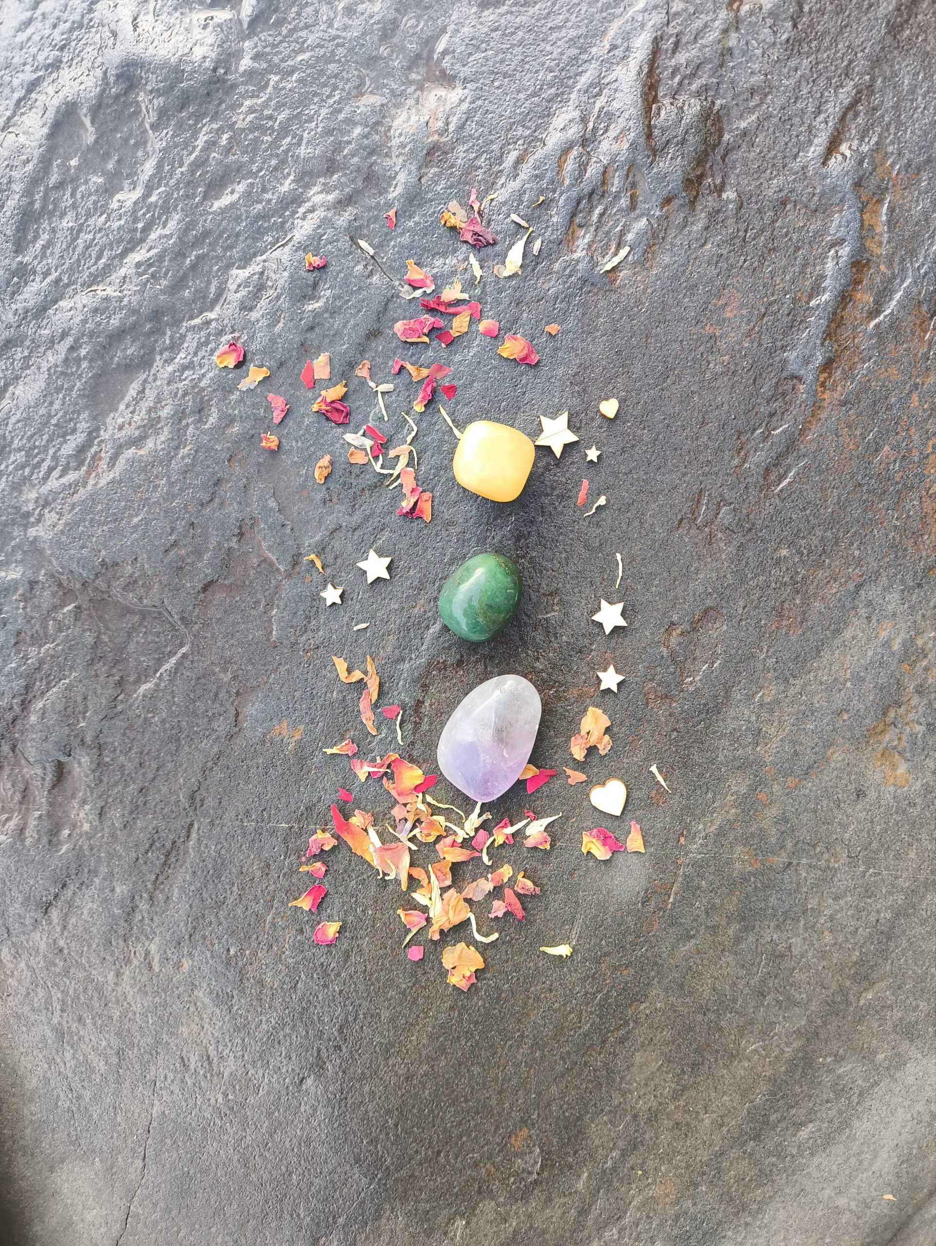 Composición simbólica con piedras pulidas de tonos amarillo, verde y violeta, dispuestas sobre superficie de piedra con pétalos y elementos decorativos