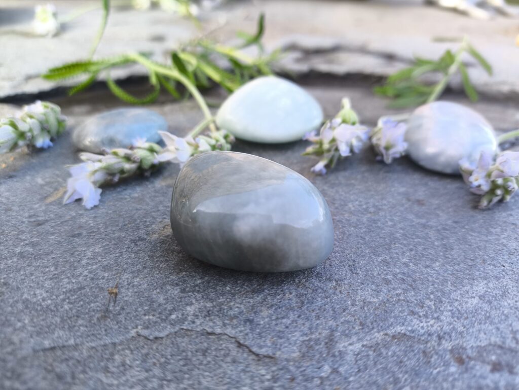Aguamarina pulida natural en tonos azul claro dispuesta junto a flores de lavanda sobre piedra