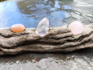 Pieza única artesanal de madera natural con piedra luna, cuarzo rosa y cuarzo pulido, composición horizontal sobre superficie de piedra