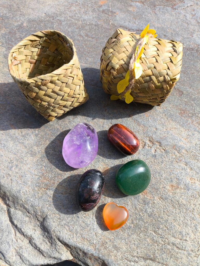 Set de piedras para Aries con granate, aventurina, ojo de toro, cornalina y amatista pulidos junto a dos cestas pequeñas sobre roca natural.