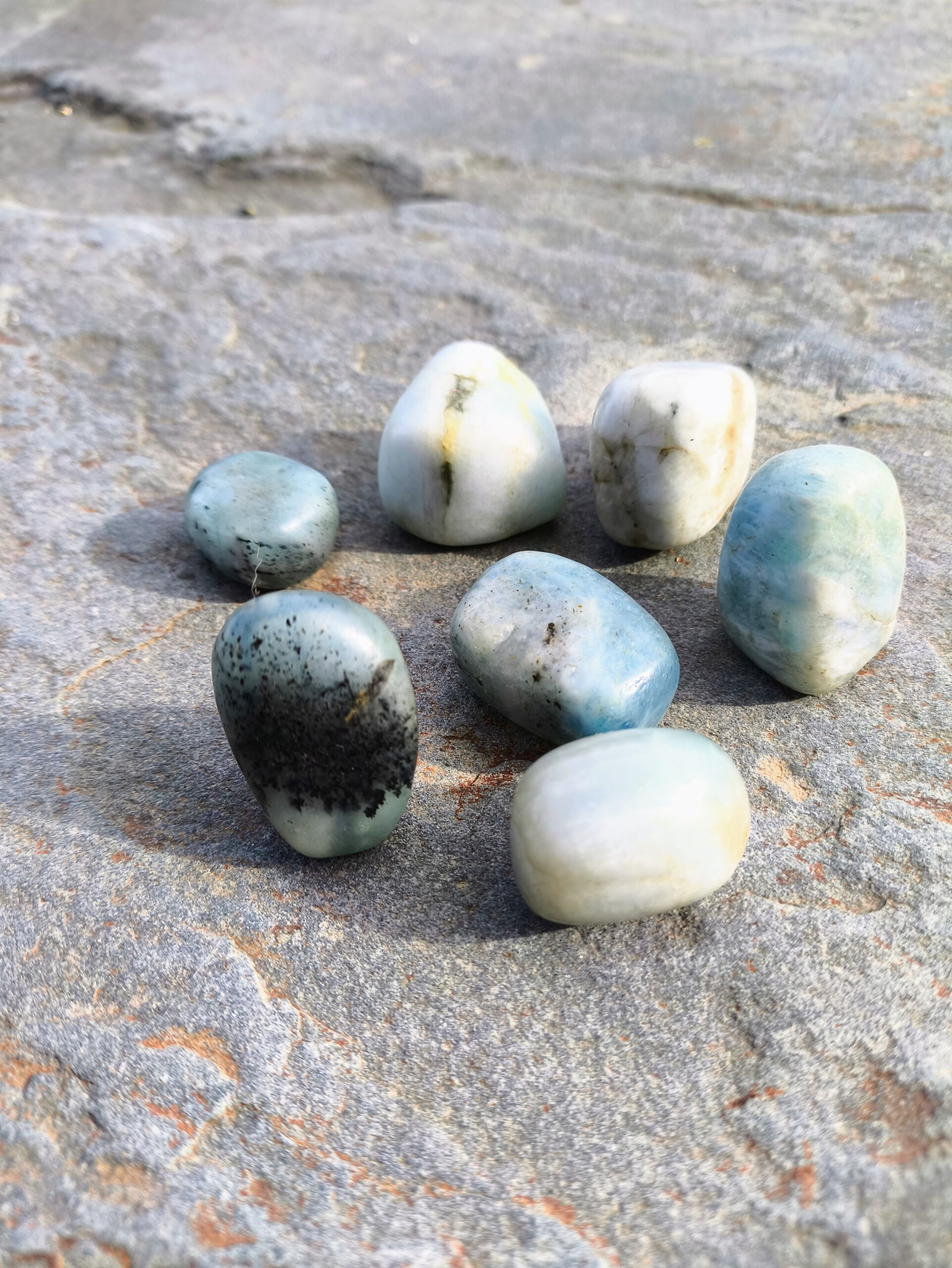 Grupo de piedras de amazonita pulida en tonos blanco y azul verdoso con vetas oscuras, colocadas sobre una roca, detalle del set de Capricornio