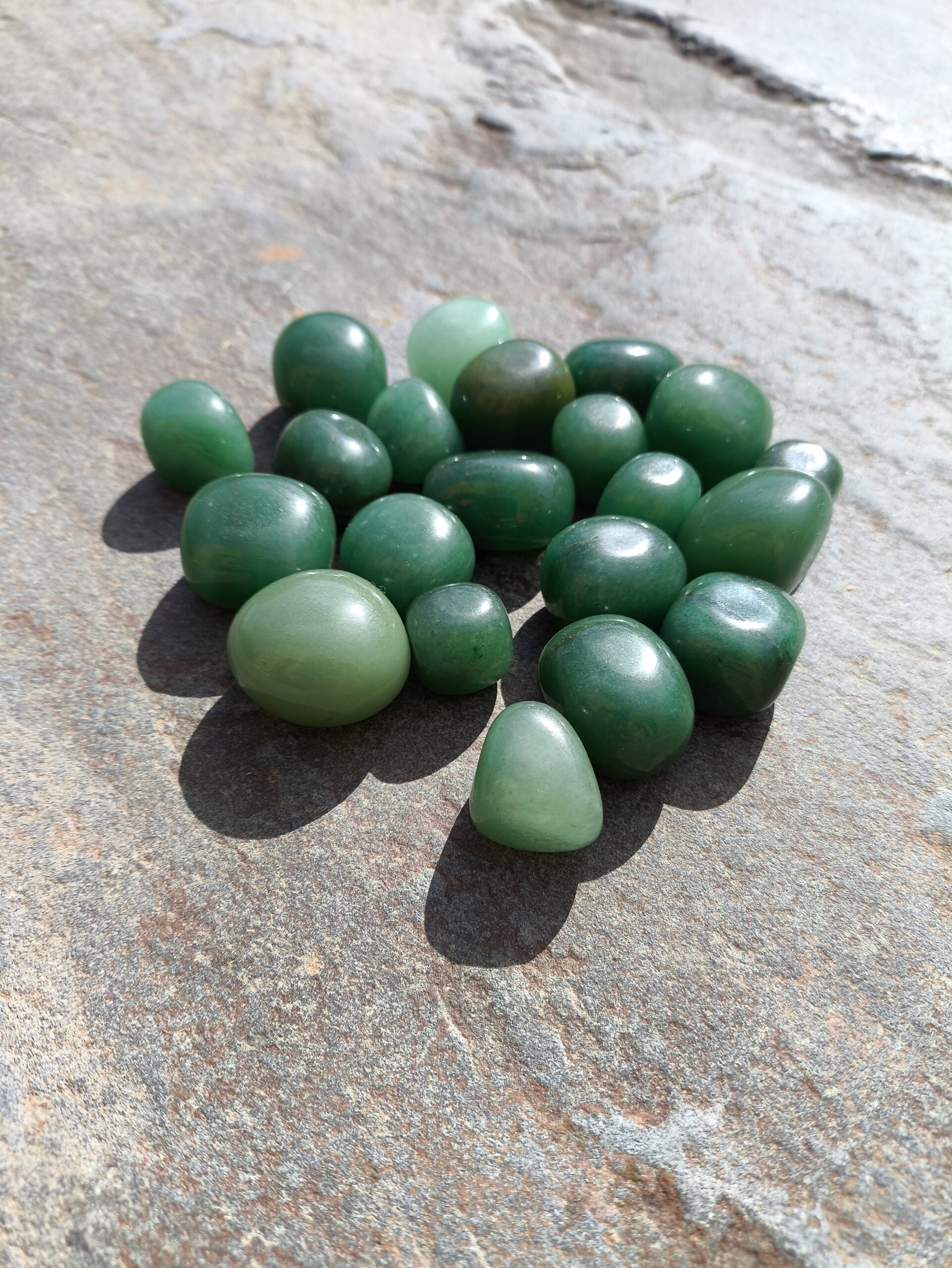Grupo de piedras de aventurina verde pulida sobre una roca iluminada por el sol, detalle del set de Capricornio