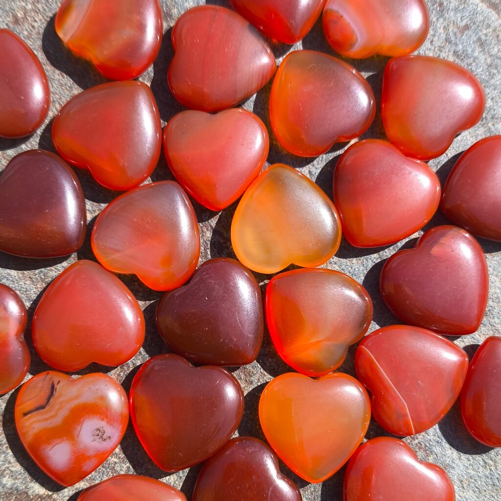 Cornalinas pulidas con forma de corazón en tonos naranja y rojo, fotografiadas sobre piedra a la luz del sol.