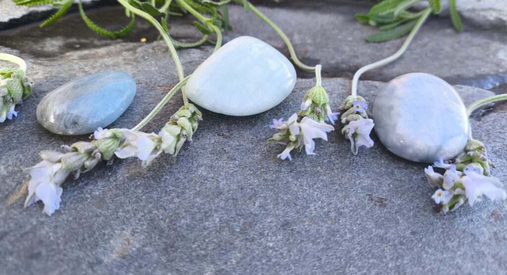 Tres aguamarinas pulidas junto a flores de lavanda sobre superficie de piedra