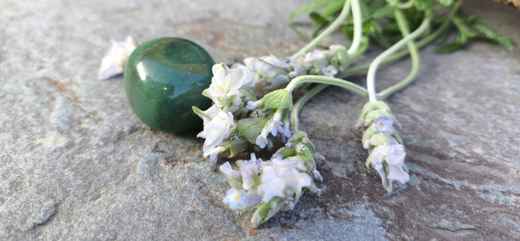 Aventurina verde pulida junto a flores de lavanda sobre una superficie de piedra, con fondo desenfocado.