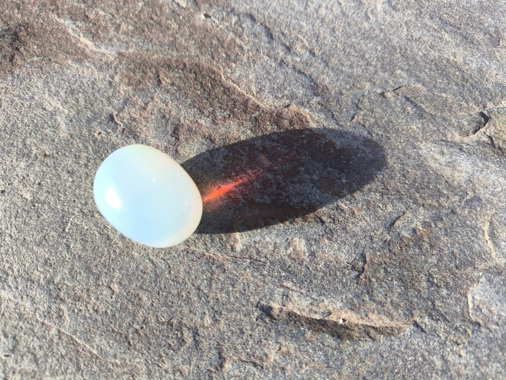 Opalita pulida sobre una roca, con luz natural y sombra alargada.