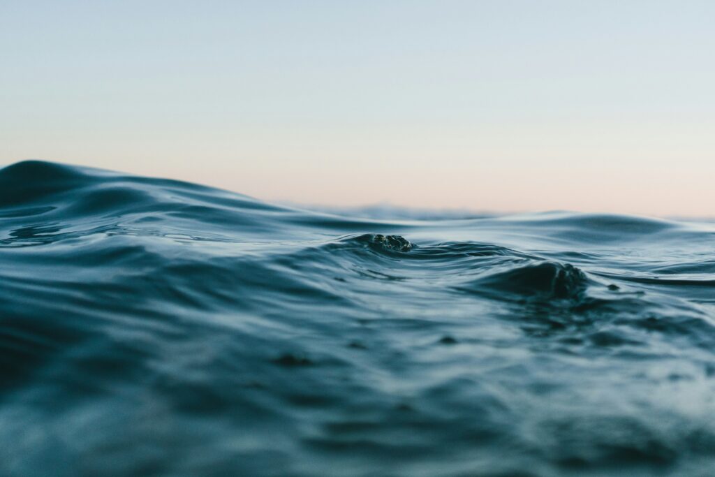 Superficie del mar en calma con pequeñas olas en primer plano y cielo suave al fondo.